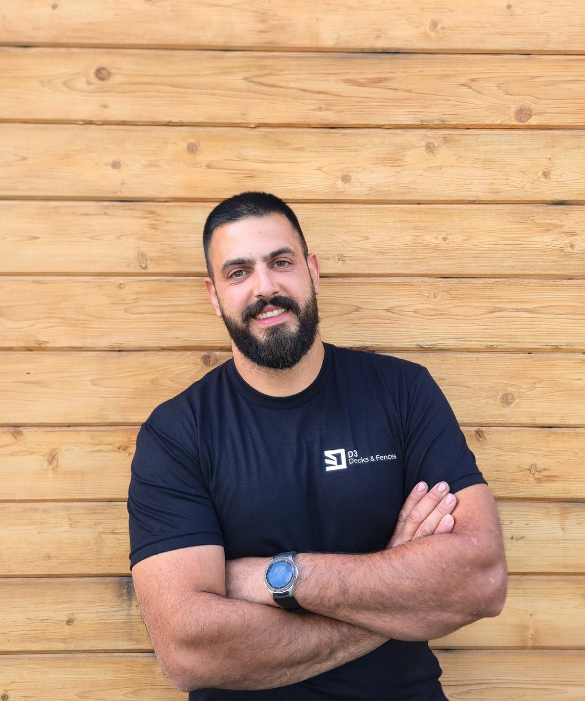 Robbie Tabet, founder of D3 Decks & Fences, standing in front of a cedar plank wall